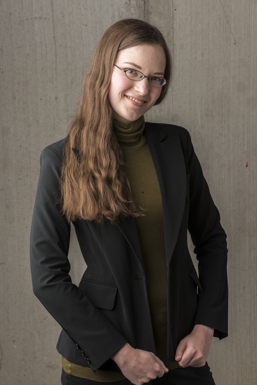 A photo of the author, a woman in her thirties with long brown hair and glasses, wearing a dark blazer.